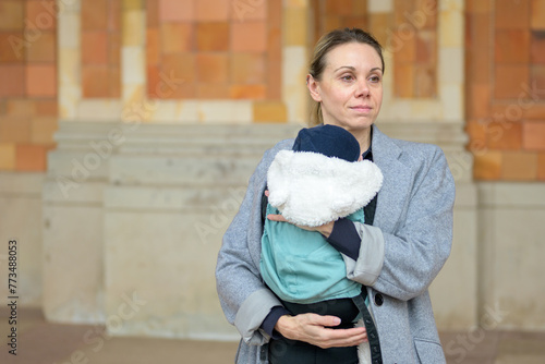 Happy late-term mother in her 40s holding her newborn baby and smiling to the side outdoor