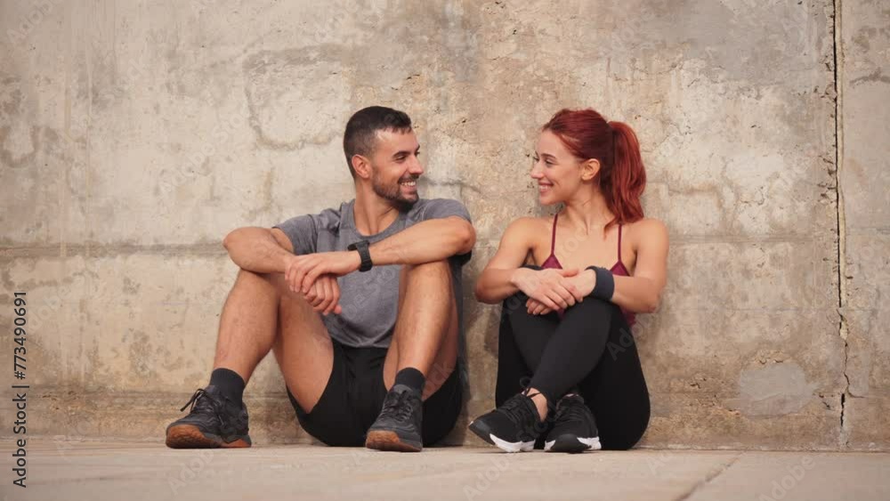 Sport couple taking a break of the workout. Tired young people looking each other, sitting on the floor, recovering energy and having a conversation. Coach man and athletic woman talking and resting Sport couple taking a break of the workout. Tired young people looking each other, sitting on the floor, recovering energy and having a conversation. Coach man and athletic woman talking and resting