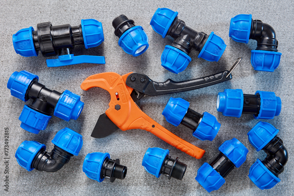 A collection of blue polyethylene pipe fittings is neatly arranged alongside an orange PVC pipe cutter, possibly during a plumbing project. A collection of blue polyethylene pipe fittings is neatly arranged alongside an orange PVC pipe cutter, possibly during a plumbing project.