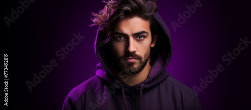 A man wearing a hoodie with the hood up standing in front of a vibrant purple background