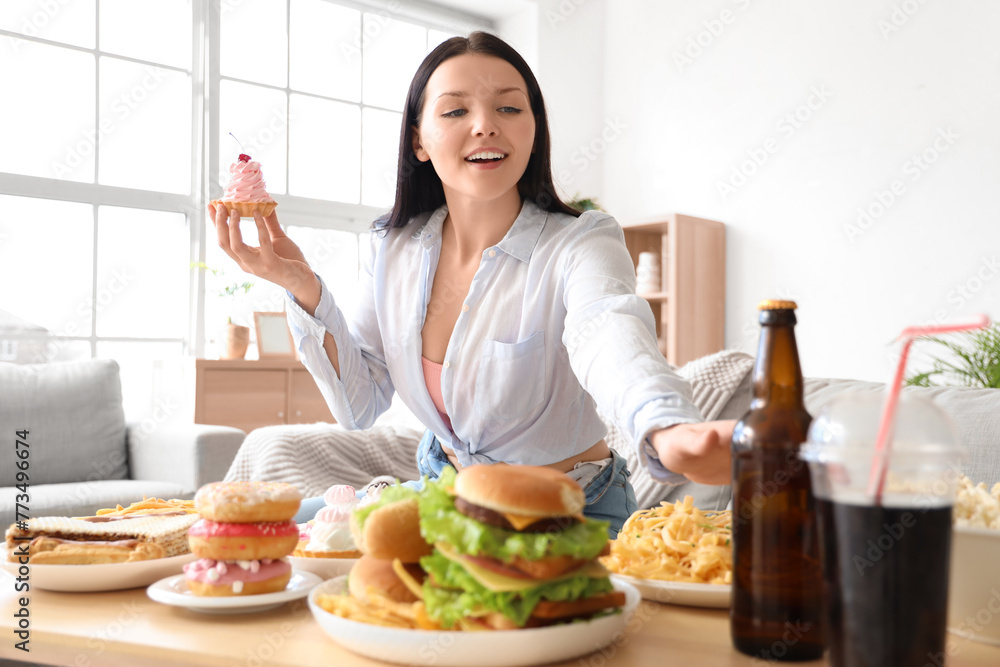 Young woman with unhealthy food on table at home. Overeating concept Young woman with unhealthy food on table at home. Overeating concept