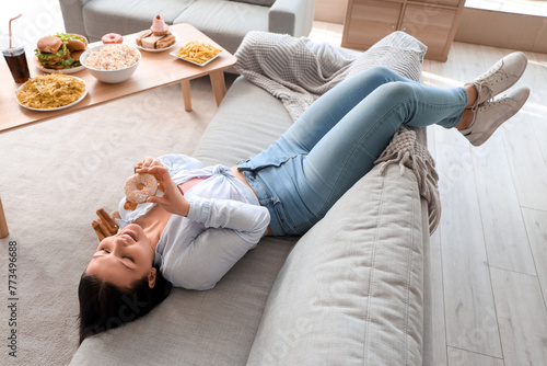 Young woman with treats lying on sofa at home. Overeating concept