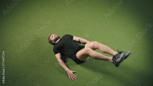 An athletic man doing leg raises on artificial turf, focused on abdominal muscle toning, within the vibrant ambiance of a modern gym. Camera 8K RAW. 