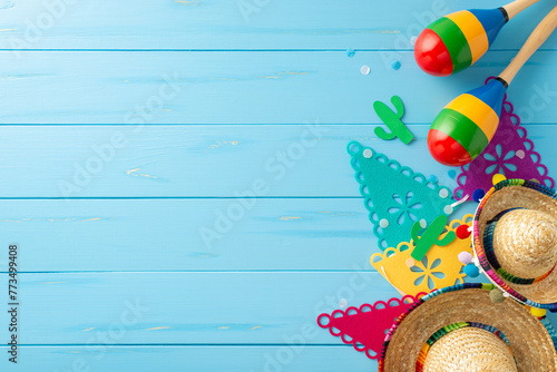 Festive Cinco de Mayo composition. Overhead view featuring symbolic items: sombreros, maracas, flag garland, and confetti on rustic blue surface. Suitable for event promotions