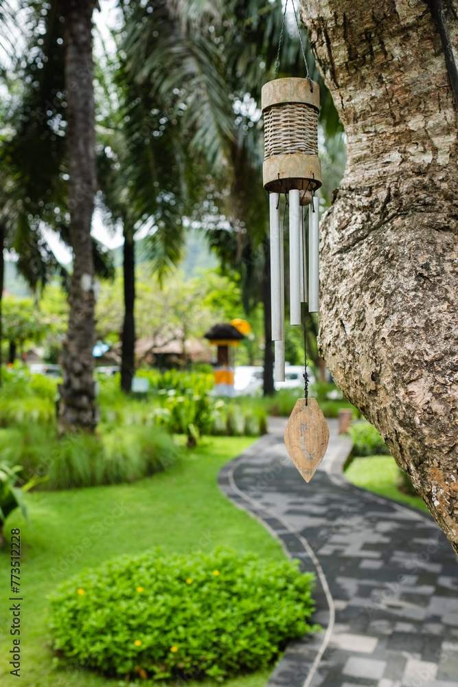 Traditional Wind Chime Hanging on a Tree in a Tropical Garden Setting with Pathway. Traditional Wind Chime Hanging on a Tree in a Tropical Garden Setting with Pathway.