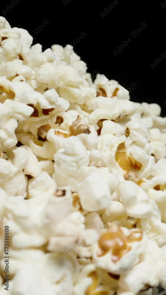 Vertical video. A large plate with a heap of popcorn rotates against a black background. Close-up. Vertical video. A large plate with a heap of popcorn rotates against a black background. Close-up.