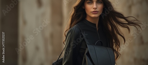 Woman with flowing long hair is elegantly dressed in a black jacket and carrying a black bag photo
