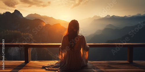 Young woman sitting on a wooden terrace and looking at the sunrise.