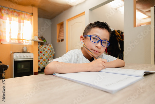 Hispanic boy writing in a notebook doing home school - 8 year old latin boy doing homework at home. Education or back to school concept