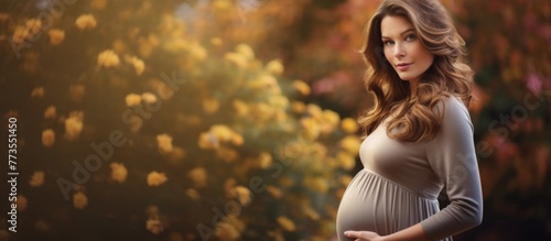 Pregnant lady standing beside a shrub with bright yellow flowers, enjoying nature photo