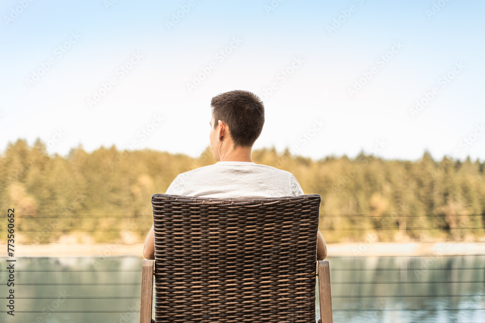 Young man sitting in chair by a lake forest enjoying time alone in nature  - obrazy, fototapety, plakaty 