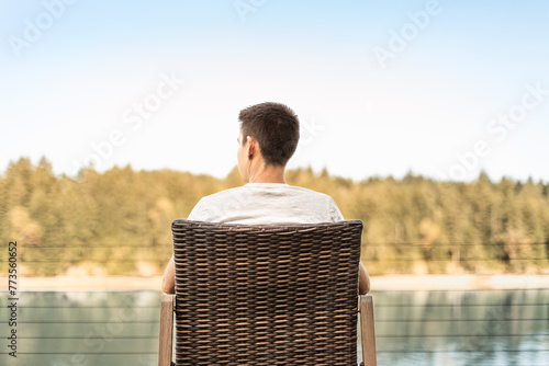 Young man sitting in chair by a lake forest enjoying time alone in nature 