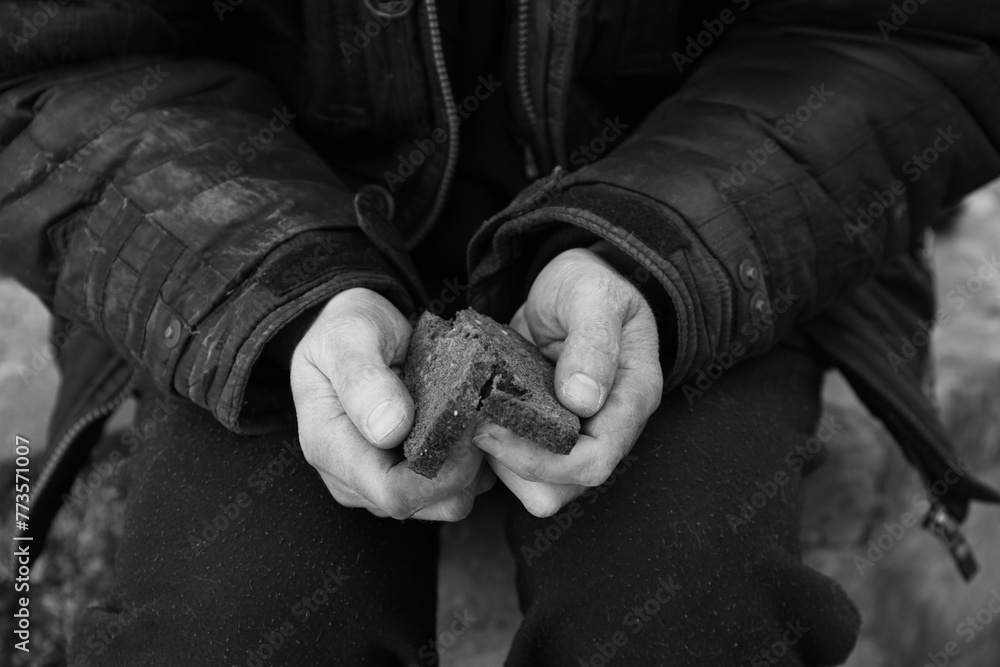 Poor homeless man holding piece of bread outdoors, closeup. Black and white effect