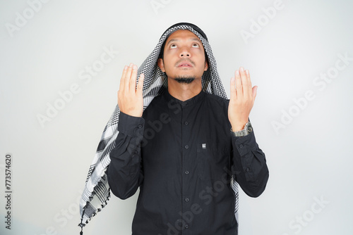 Asian muslim man is praying with hands up, wearing Arab turban sorban in copy space isolated photo