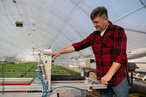 Man working on automatic hole tray sowing seeder , greenhouse in the background  photo