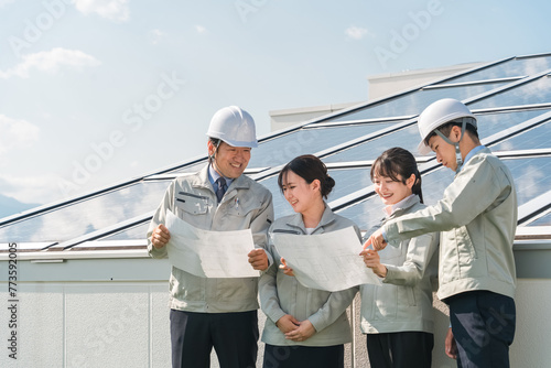 太陽光発電・ソーラーパネルの前に立つ電力会社・電気工事業者の作業着姿の技術者（クリーンエネルギー）
 photo