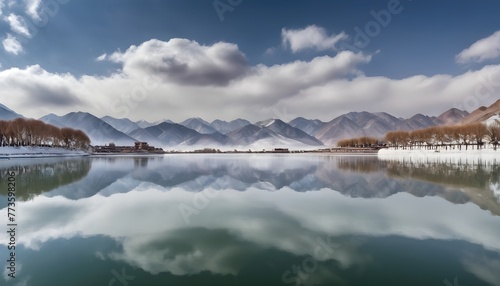 In the winter, there is heavy snow on both sides of West Lake in China's Gansu Province with snowy mountains and a cloudy sky in the distance. The lake water reflects white clouds like mirror reflecti photo