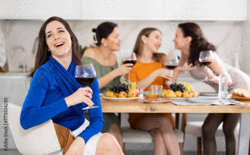 Laughing brunette with glass of red wine enjoying fun gathering with female friends at cozy house party