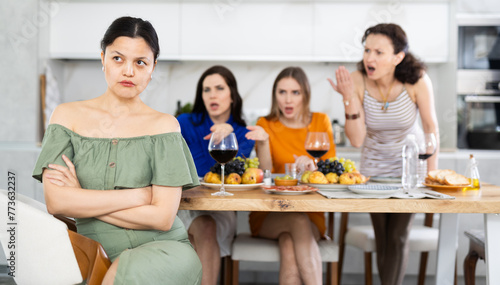 At home party  young Asian woman appearing offended and upset during argument while female friends in background showing disapproval and discontent..