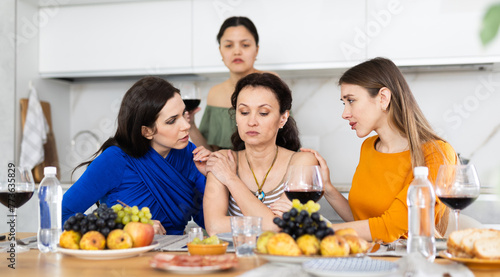At cozy home gathering  attentive female friends comforting and supporting upset woman  discussing problems and giving advice over glass of wine