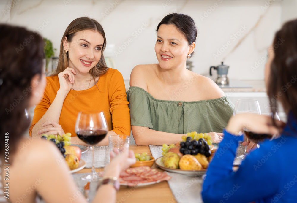 Group of women friends talking and drinking wine at party in kitchen
