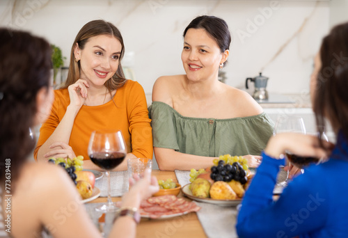 Group of women friends talking and drinking wine at party in kitchen
