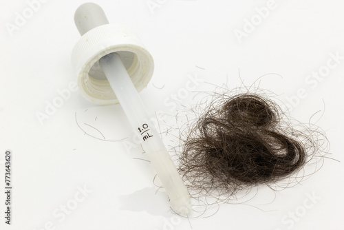 Minoxidil hair treatment dropper next to a pile of brown hair on a white background. This image can be used to illustrate topics related to hair loss, medical treatments and aging.  (ID: 773643620)