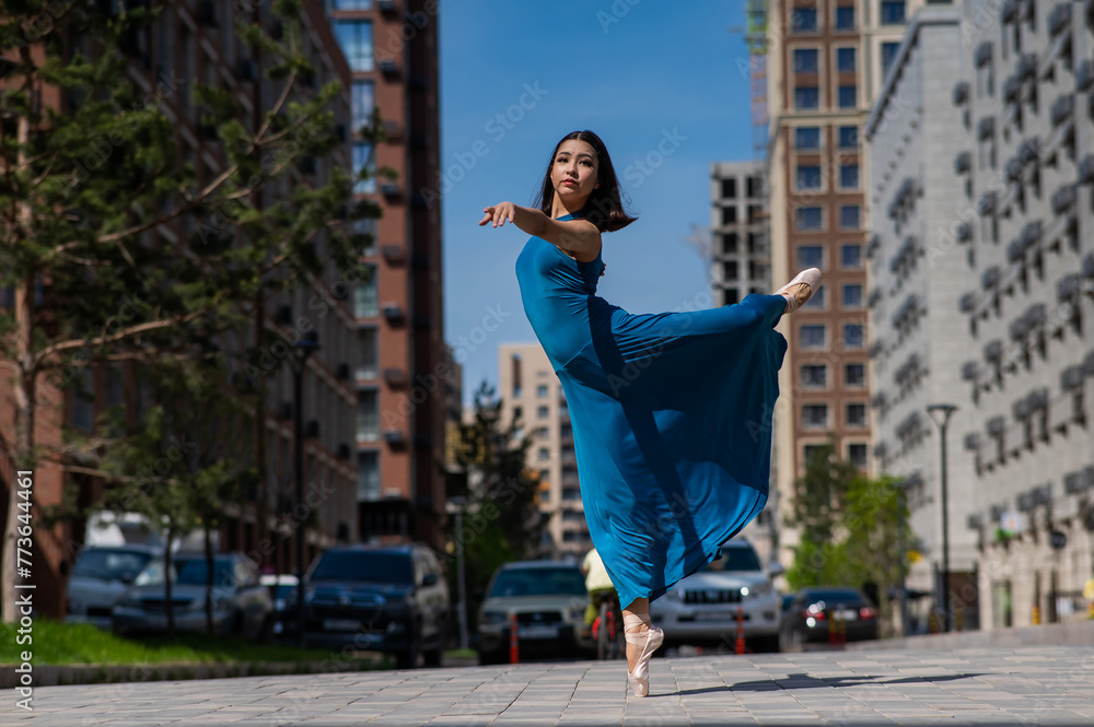 Beautiful Asian ballerina in blue dress dancing outdoors. Urban landscape.