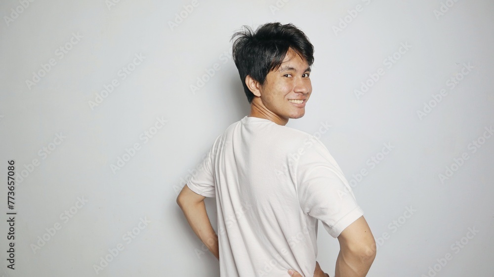 Asian young man smiling posing from his back looking forward as if turning his body Asian young man smiling posing from his back looking forward as if turning his body