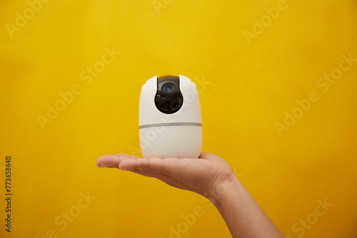 A hand hold a wireless security camera on yellow background 