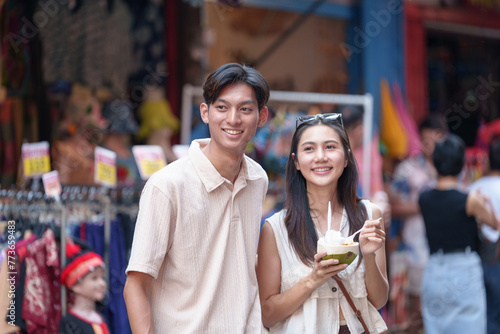 Tourist Asian couple walking around the market while eating Fruits from street stalls in the city market and crowds of people in the streets  alleys  tourist towns.