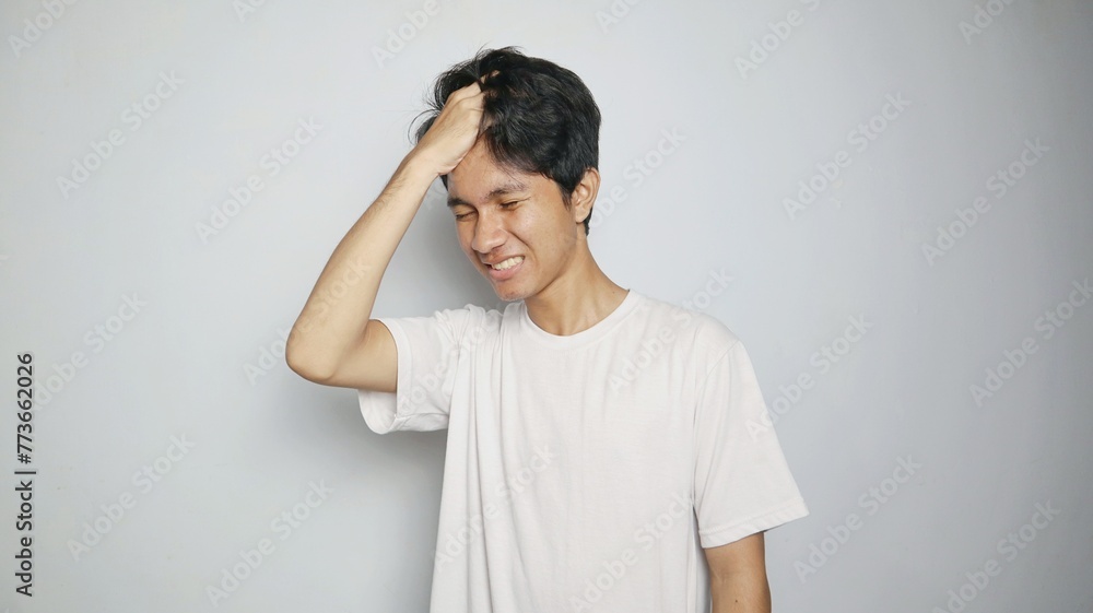 Young Asian man in white shirt gesturing with hand holding head, feeling dizzy, sick, stressed, depressed Young Asian man in white shirt gesturing with hand holding head, feeling dizzy, sick, stressed, depressed