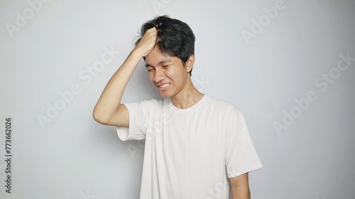 Young Asian man in white shirt gesturing with hand holding head, feeling dizzy, sick, stressed, depressed