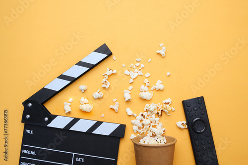 Clapperboard, popcorn and remote control on yellow background