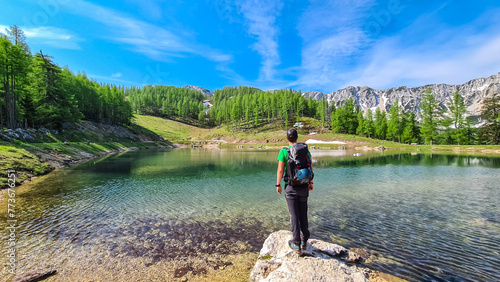 Hiker man at alpine lake with panoramic view of mountain peaks Feistritzer Spitze (Hochpetzen) and Kriznik, Karawanks, Carinthia, Austria. Wanderlust Austrian Alps. Hiking trail on Petzen, Bleiburg photo