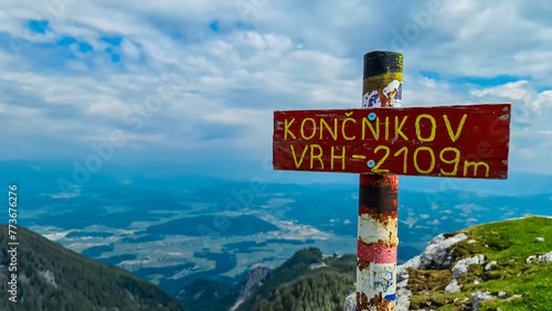 Sign indicating top of mountain peak Kriznik, Carinthia, border Austria Slovenia. Alpine meadow with scenic view of mountain range Karawanks, Slovenian Austrian Alps. Hiking trail on Petzen, Bleiburg photo