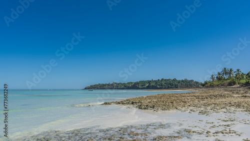 Tropical seascape. Low tide. The rocky seabed was exposed. A boat in the turquoise ocean. Green vegetation in the distance. Clear blue sky. Copy space. Madagascar. Nosy Iranja   
