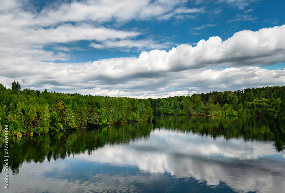 A tranquil summer landscape with a crystal-clear lake reflecting the blue sky and fluffy white clouds, surrounded by lush green trees A tranquil summer landscape with a crystal-clear lake reflecting the blue sky and fluffy white clouds, surrounded by lush green trees