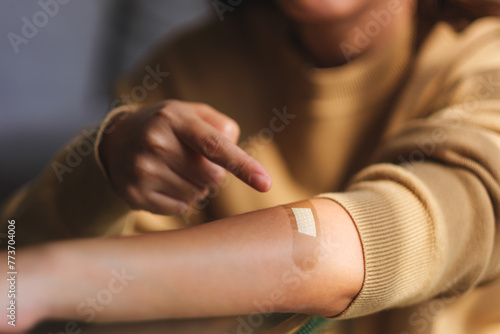 Closeup image of a young woman pointing finger at a adhesive bandage, medical plaster, band aid on her arm photo
