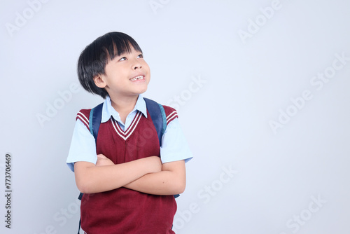 Smart Asian schoolboy wearing backpack and looking up to empty space