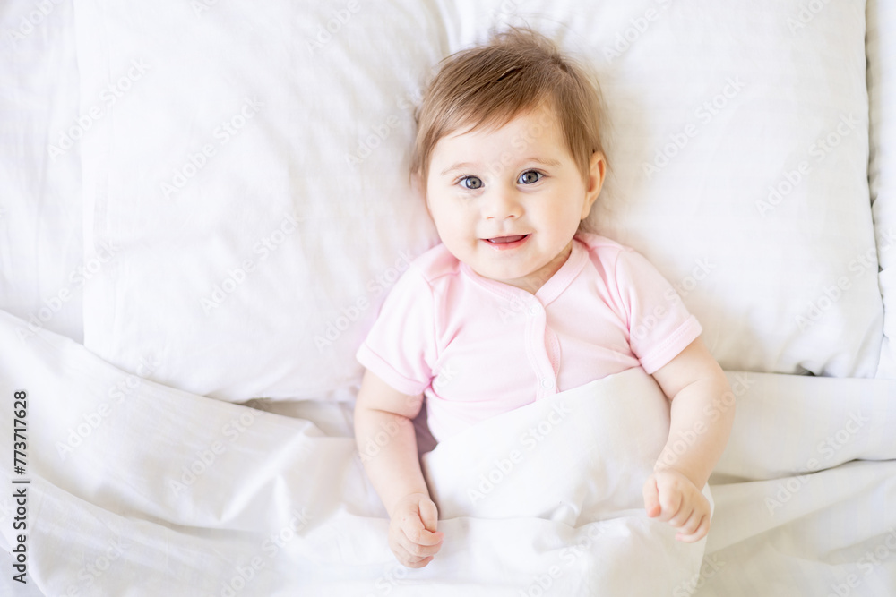 baby newborn girl on a white crib in a bright bedroom close-up in pink clothes smiling or laughing, place for text, top view baby newborn girl on a white crib in a bright bedroom close-up in pink clothes smiling or laughing, place for text, top view