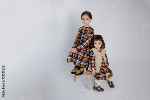 two little sisters, 6 and 3 years old, in stylish identical dresses, have fun and play on a studio cyclorama during a photo shoot