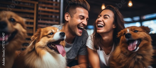 A man and a woman are seated on the ground with their pet dogs, sharing a happy moment as they all laugh together