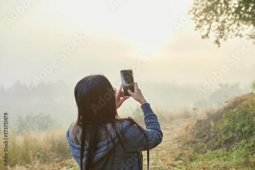 Rear view of woman holding smartphone and taking misty morning
