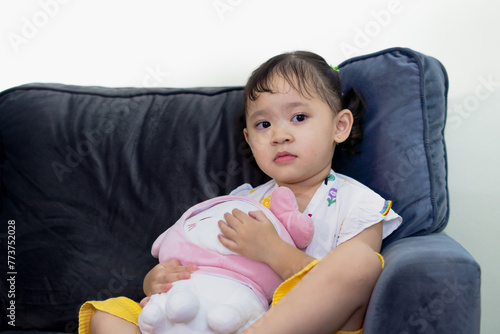 Happy cute toddler sitting on sofa, holding doll, facing camera in living room. photo