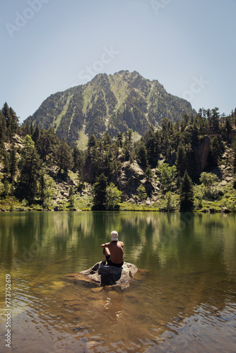 Man sitting in a lake with a forest and a mountain in the background