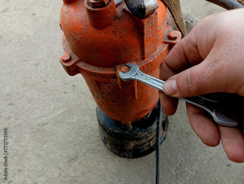 Repair of a hydraulic pump for pumping out water. A man repairs an orange water pump with a wrench. photo