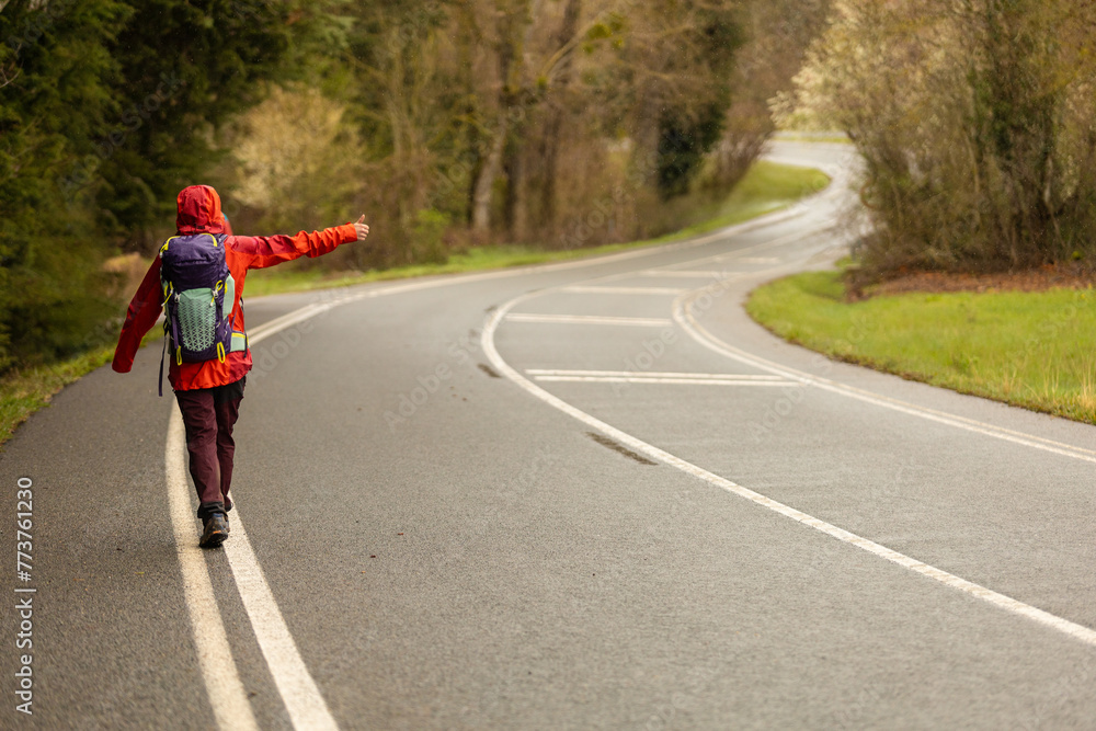 A person is walking on a road with a backpack and pointing to the right