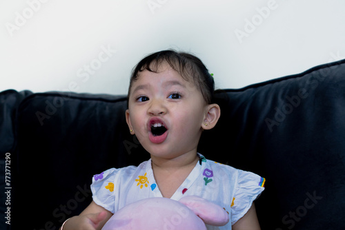 Happy cute toddler sitting on sofa, holding doll, facing camera in living room. photo