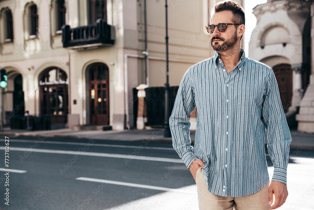 Portrait of handsome confident stylish hipster lambersexual model. Sexy modern man dressed in blue shirt and trousers. Fashion male posing on street background in Europe city at sunset, sunglasses Portrait of handsome confident stylish hipster lambersexual model. Sexy modern man dressed in blue shirt and trousers. Fashion male posing on street background in Europe city at sunset, sunglasses